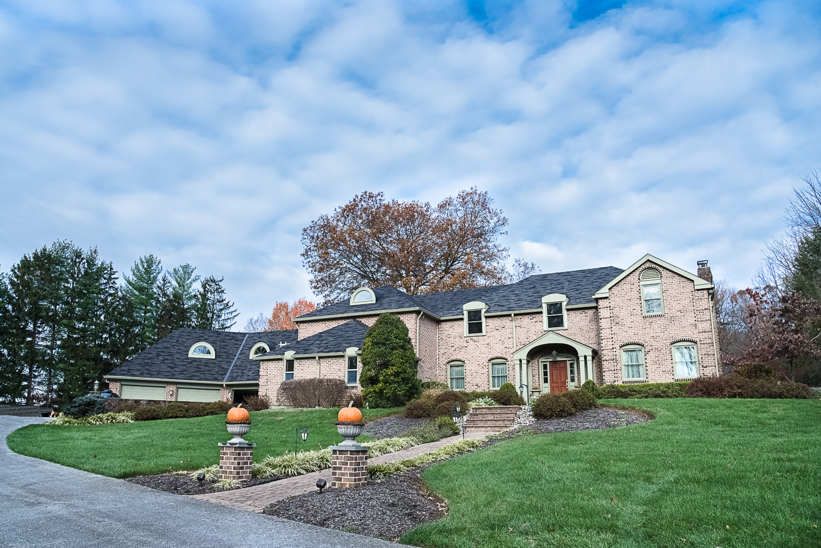 Large brick house with a well-maintained lawn, autumn trees, and a cloudy sky.