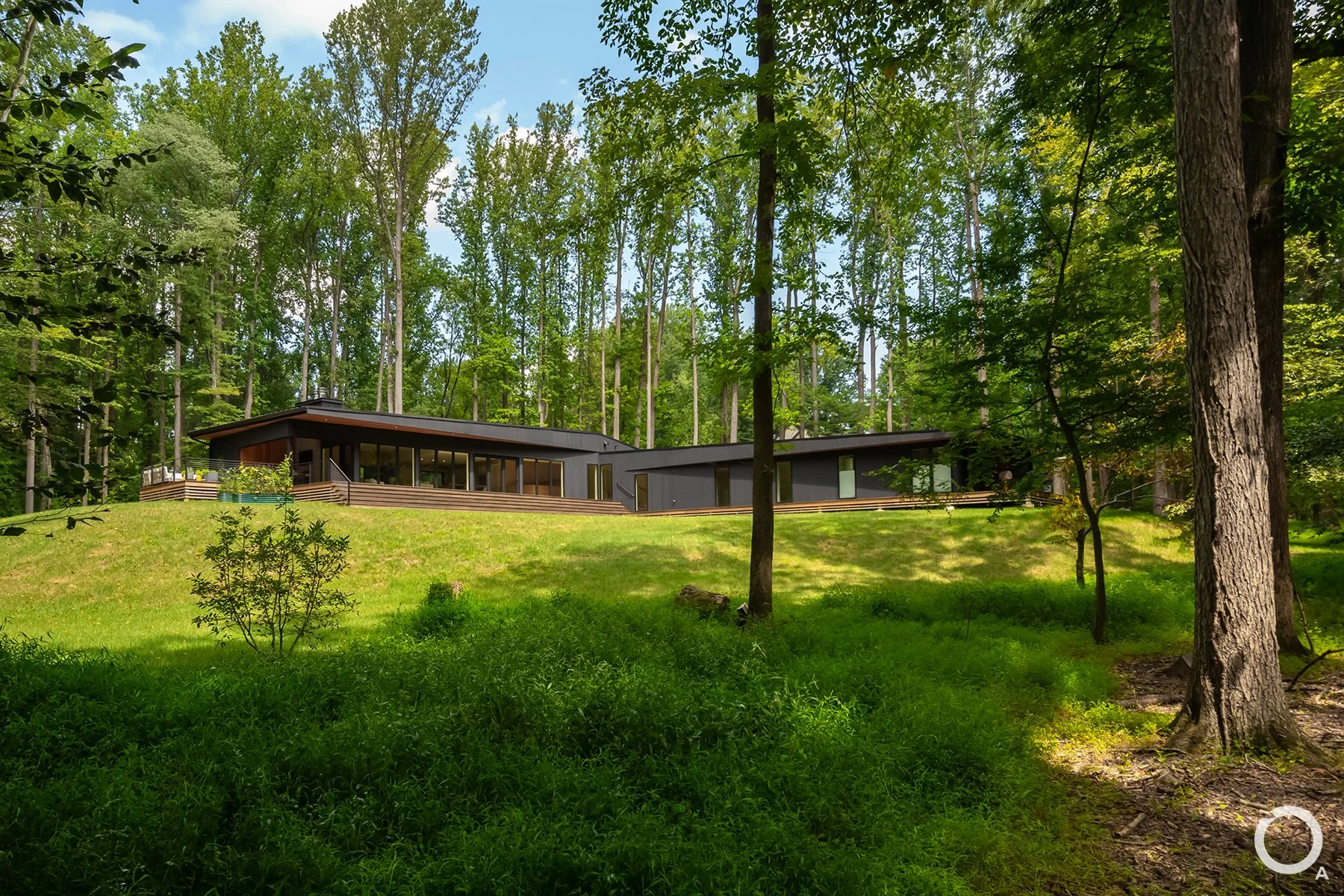 Modern L-shaped custom home with dark exterior cladding, expansive glazing, and a low-profile roof on a wooded site in Chadds Ford, Pennsylvania.  Photo Credit: Linda McManus Photography