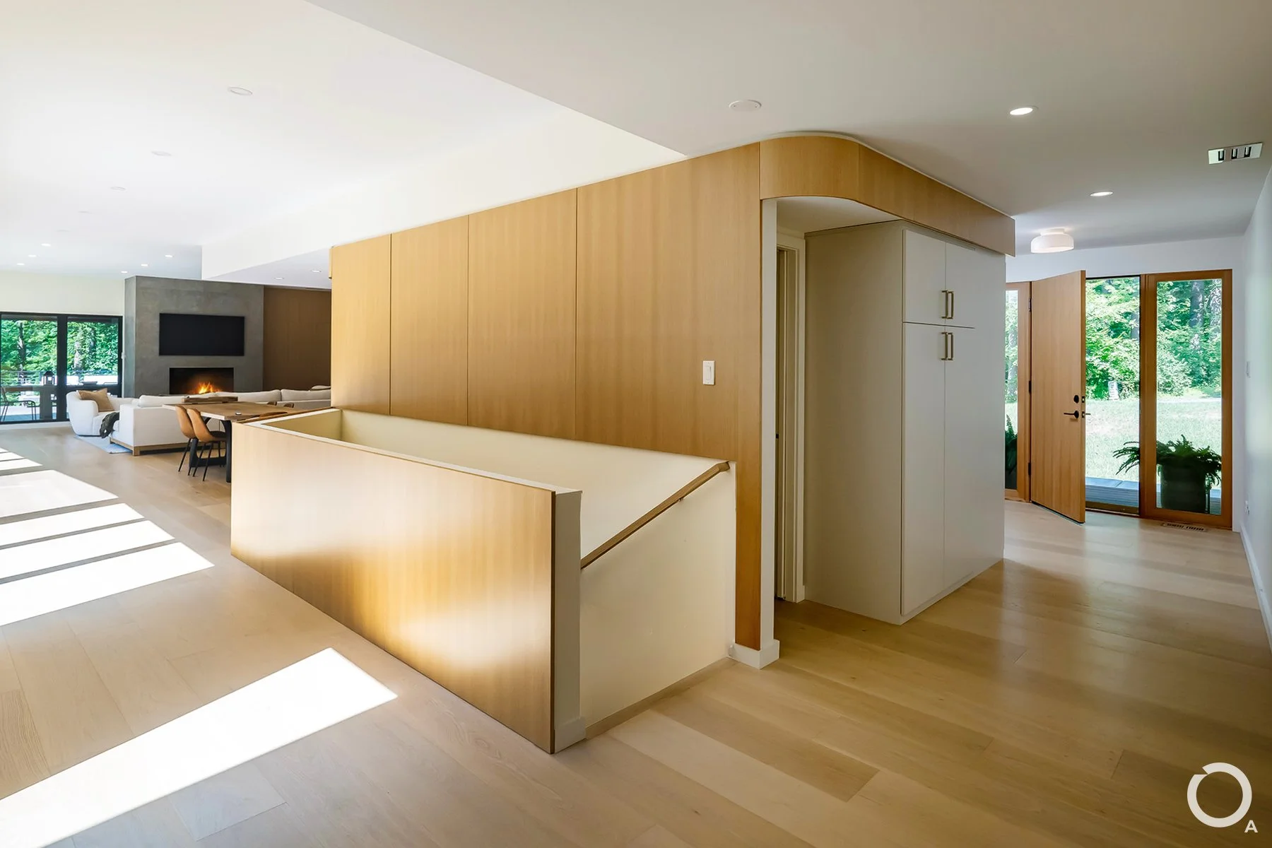 Contemporary entry hall with a curved wood-paneled partition, integrated storage, light hardwood flooring, and views toward the living room. Photo Credit: Linda McManus Photography