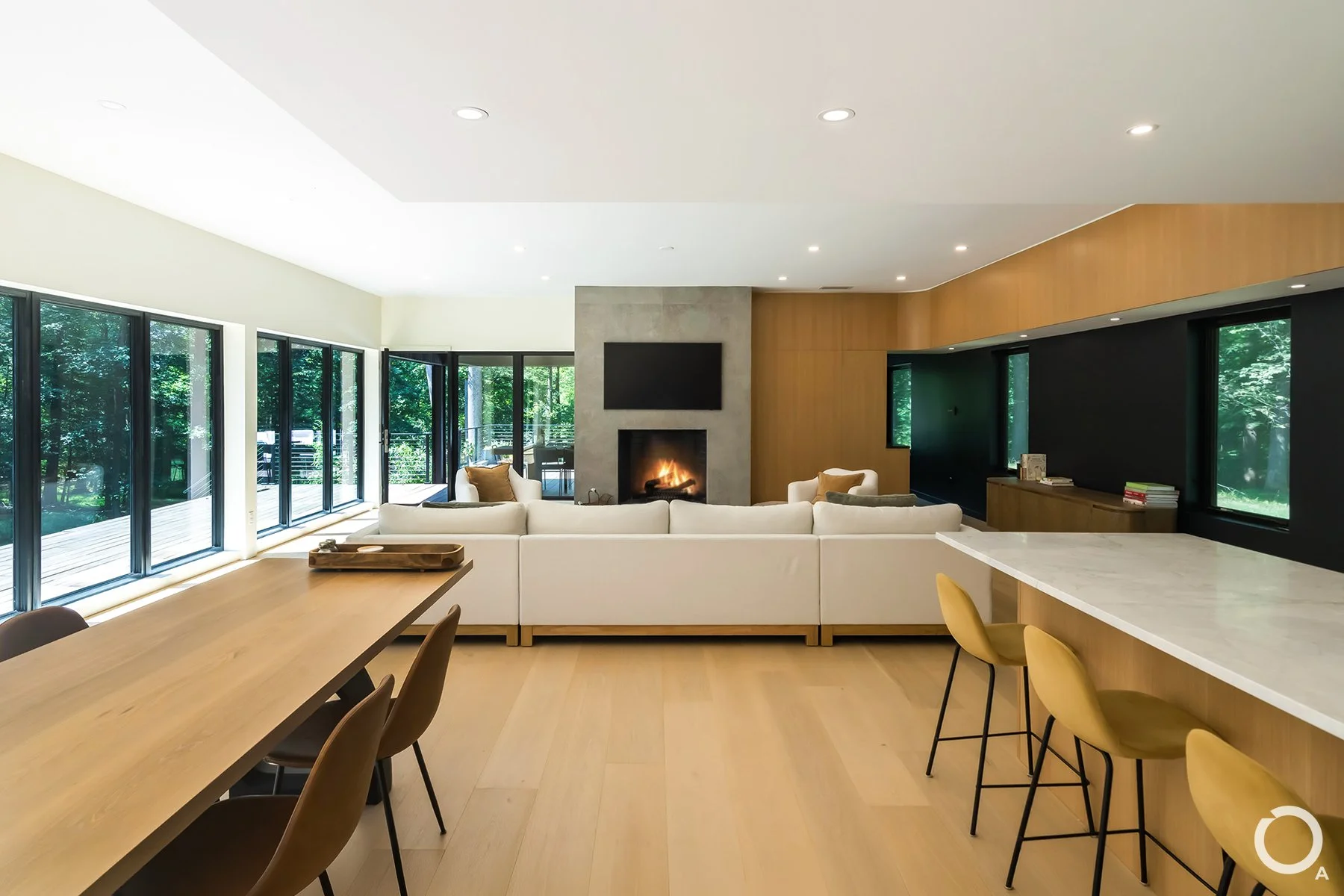 Contemporary living room with a concrete fireplace, white sectional sofa, natural wood finishes, and folding glass doors opening onto a terrace. Photo Credit: Linda McManus Photography