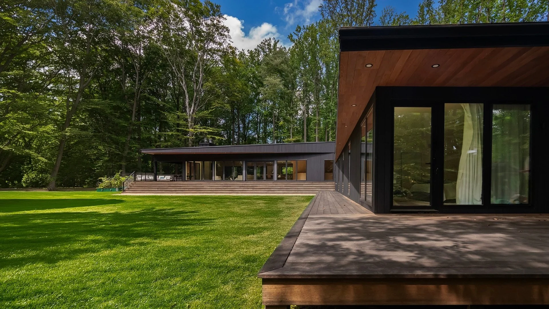 Modern Timber Ridge House in Chadds Ford, PA, designed by ONY Architecture, featuring a covered wood deck, deep timber soffits, and glazing overlooking the wooded landscape.