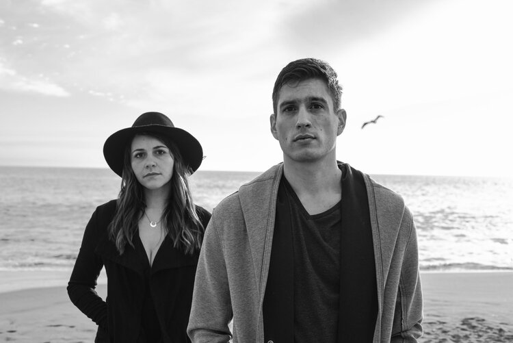 Casey Wickstrom and Taylor Rae pose for a photo in front of the ocean.