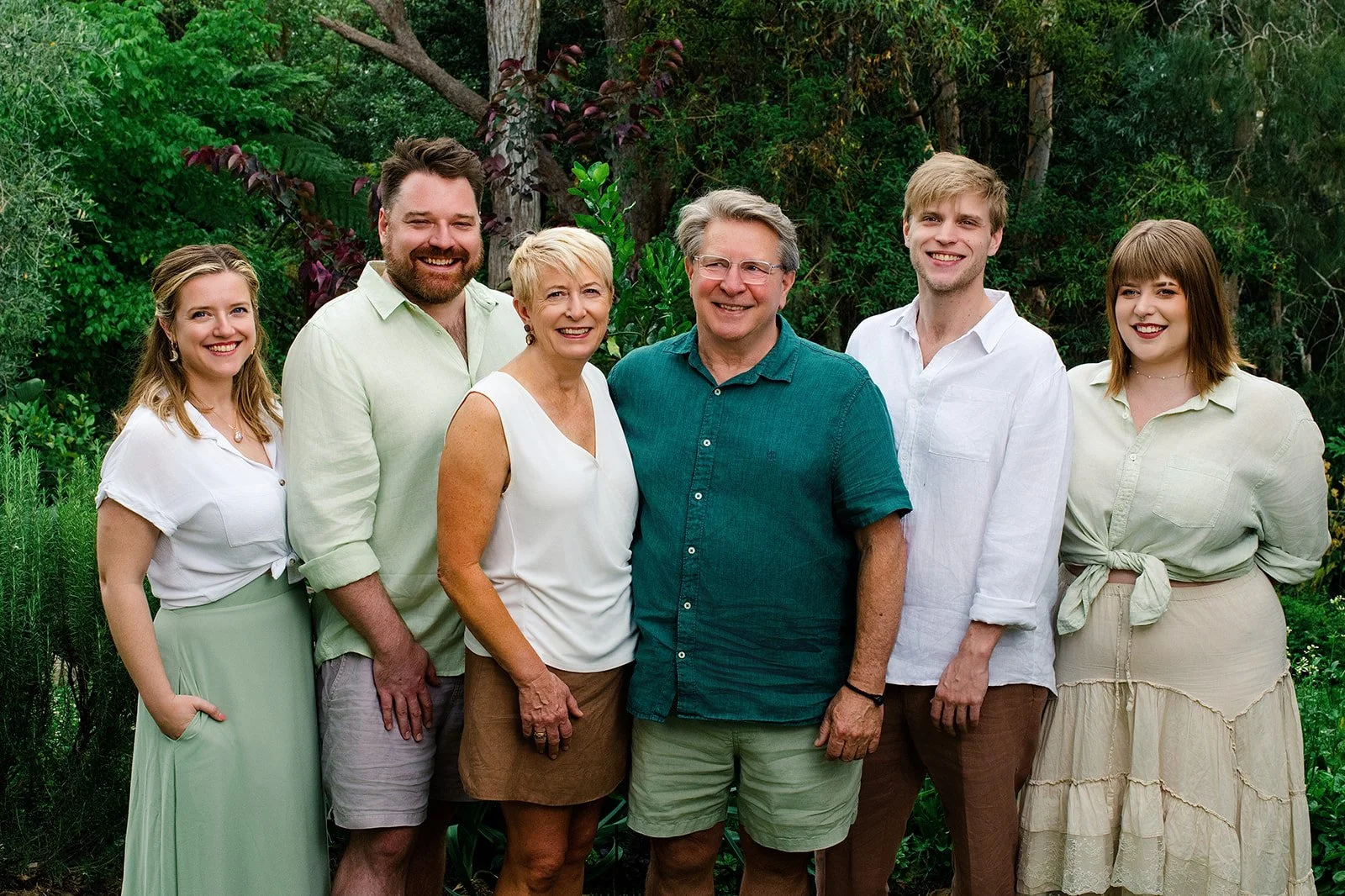 A well dressed family standing smiling at the camera with the Australian bush behind