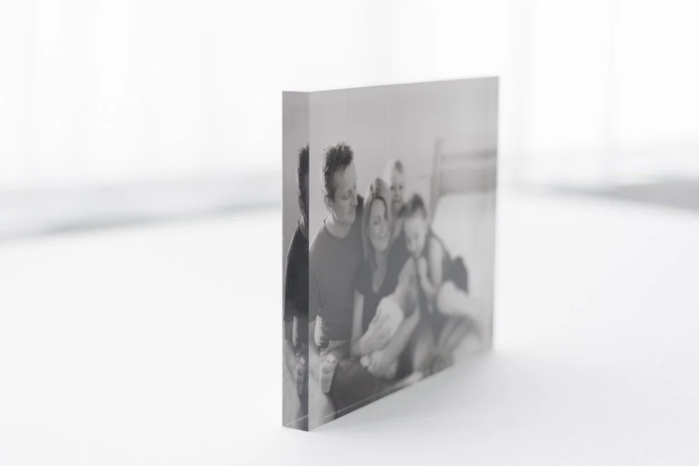 A black and white photo displayed on a small square acrylic block, showing a family of four sitting together and smiling.