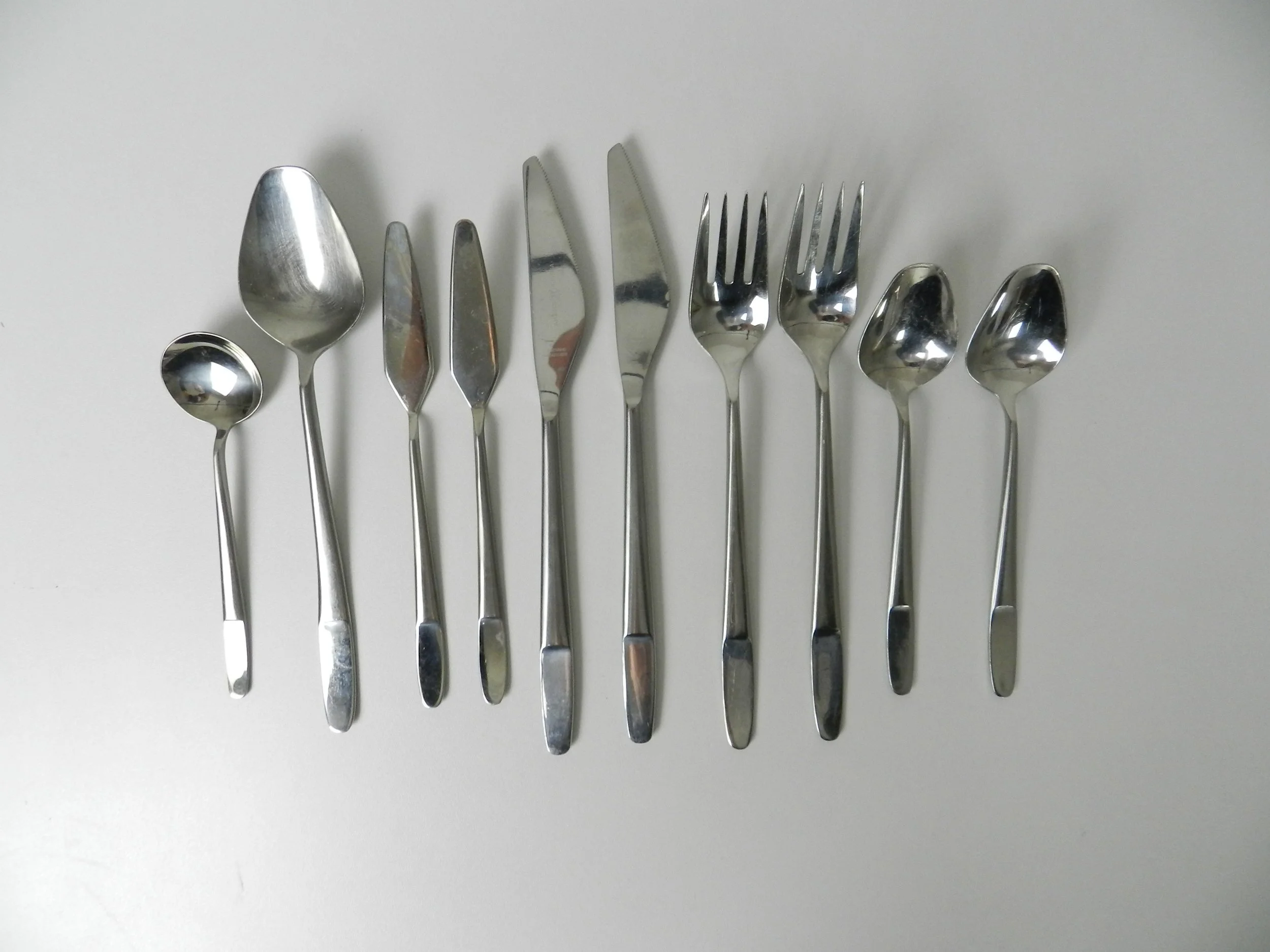 Modernist stainless steel flatware set (model 2070) designed by Helmut Alder for Amboss. Six piece place settings for 10 plus 10 extra pieces, total of 70.  Austria, 1960s.