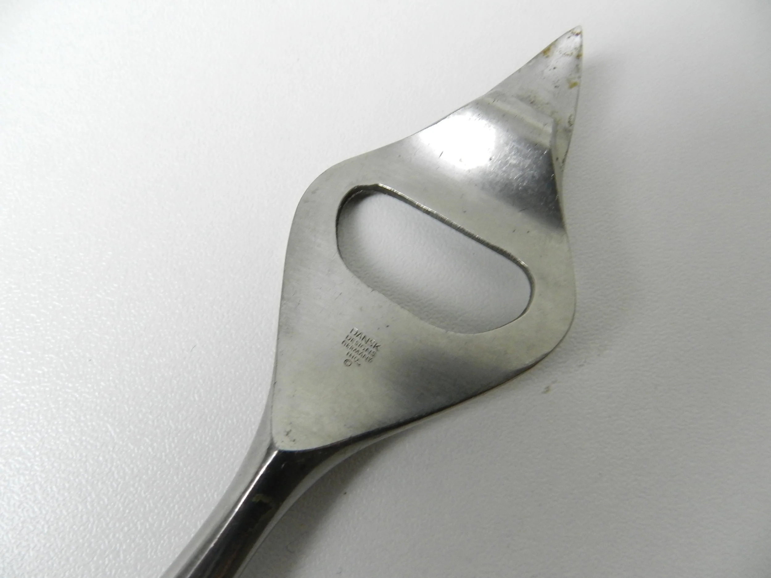 Fjord can/bottle opener designed by Jens Quistgaard for Dansk. Stainless steel with teak handle.  Germany, 1960s.