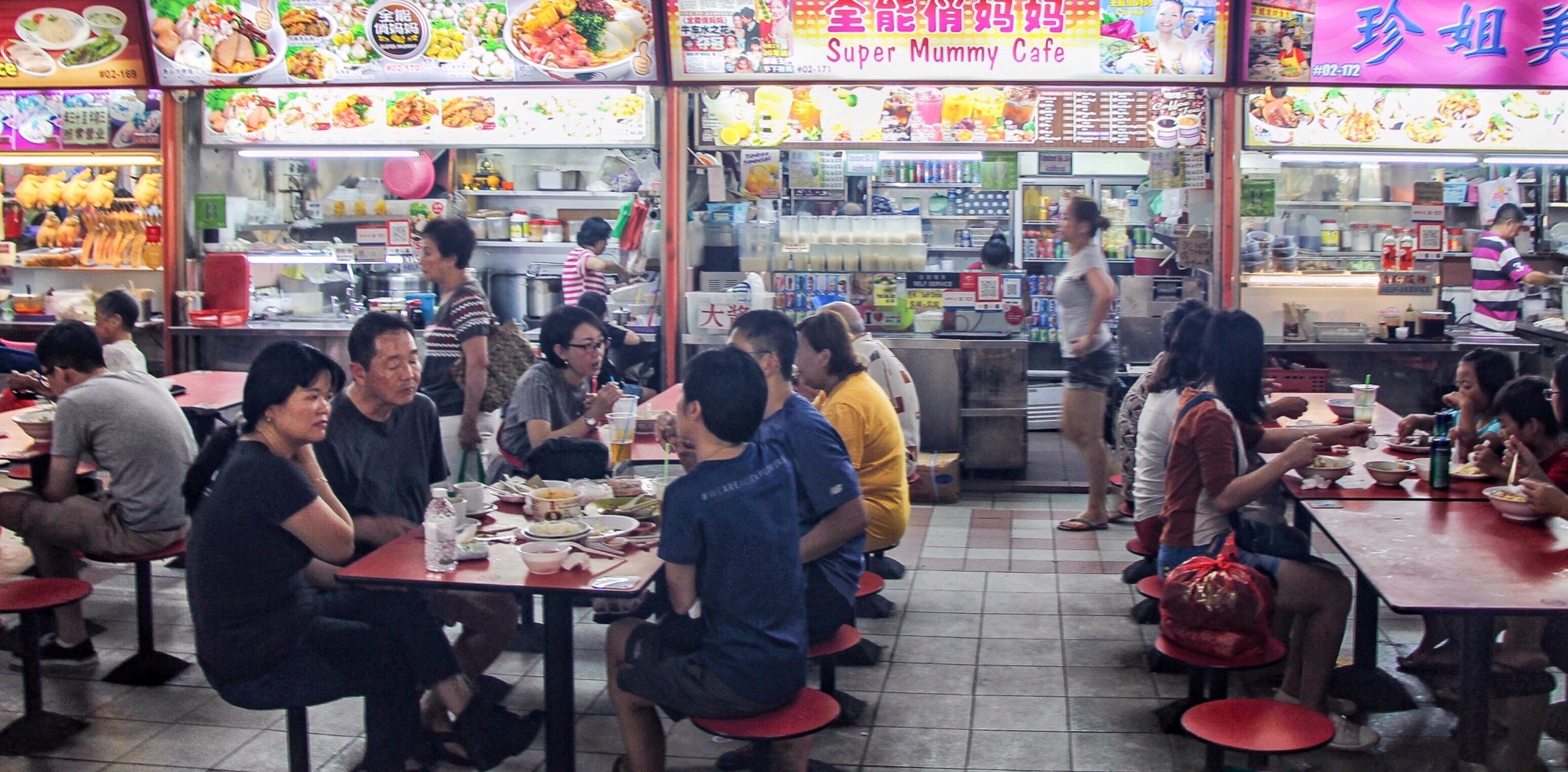 Brightly lit signboards illuminate diners meals at the hawker stalls in Chinatown Food Centre. Each stall displays vibrate photographs of their specialty dish.