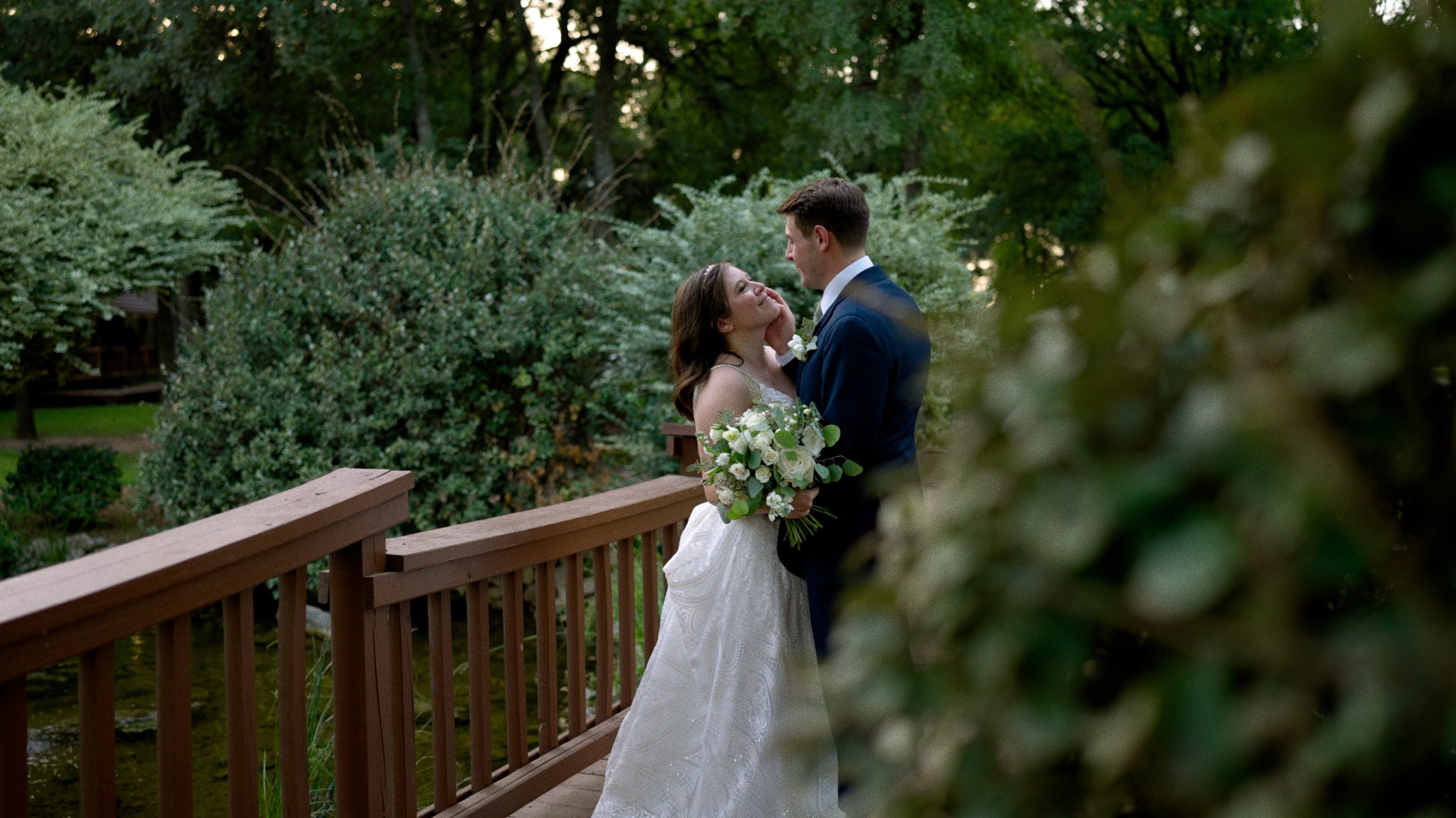 bride and groom posing on bridge in love through bushes