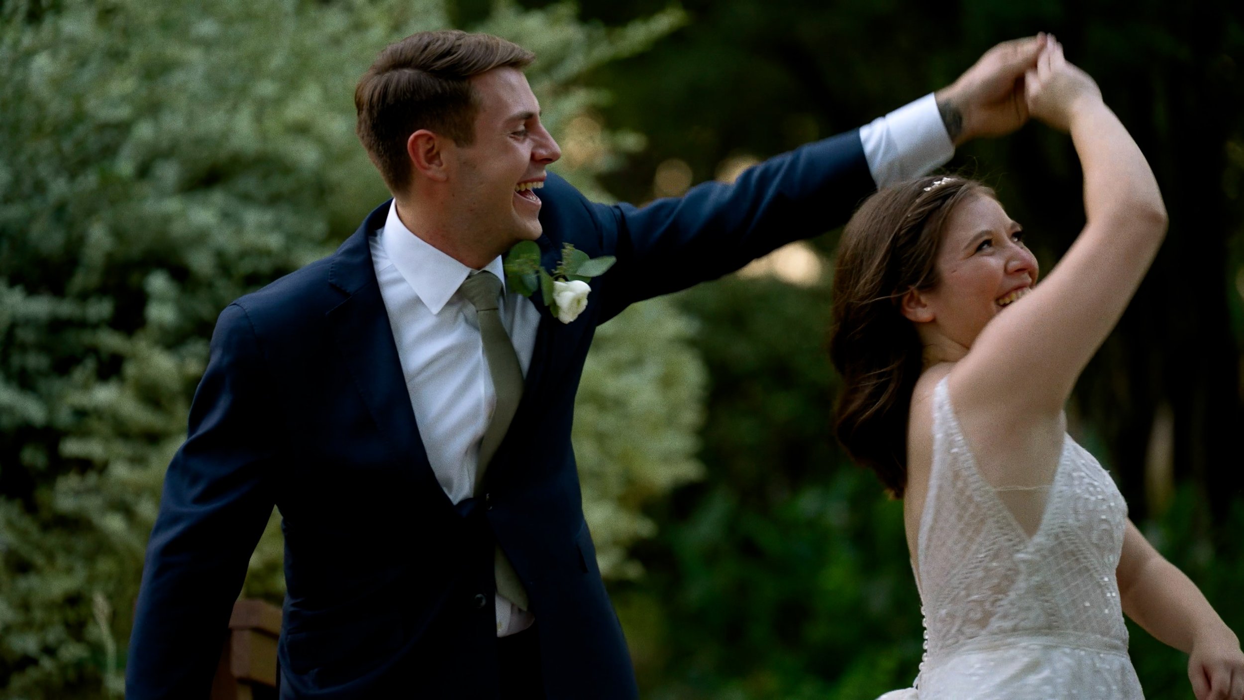 groom spins bride dancing laughing on bridge outside sunset