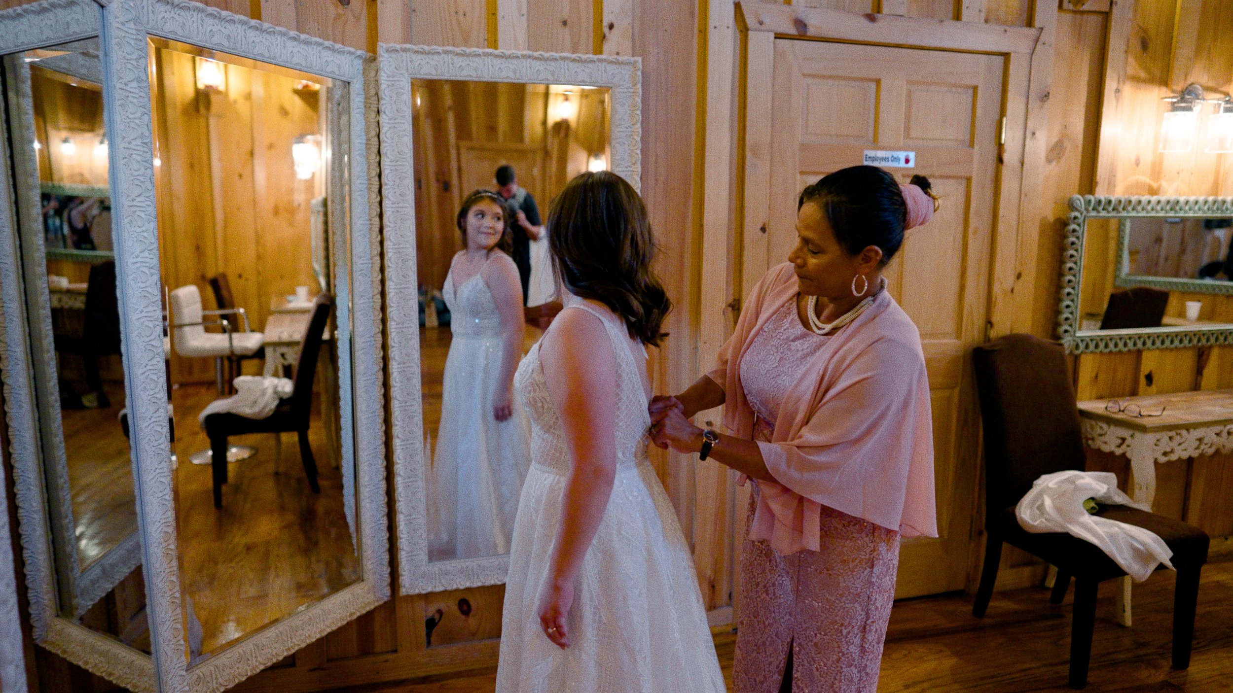 mother of bride helps bride get in wedding dress looking in mirrors