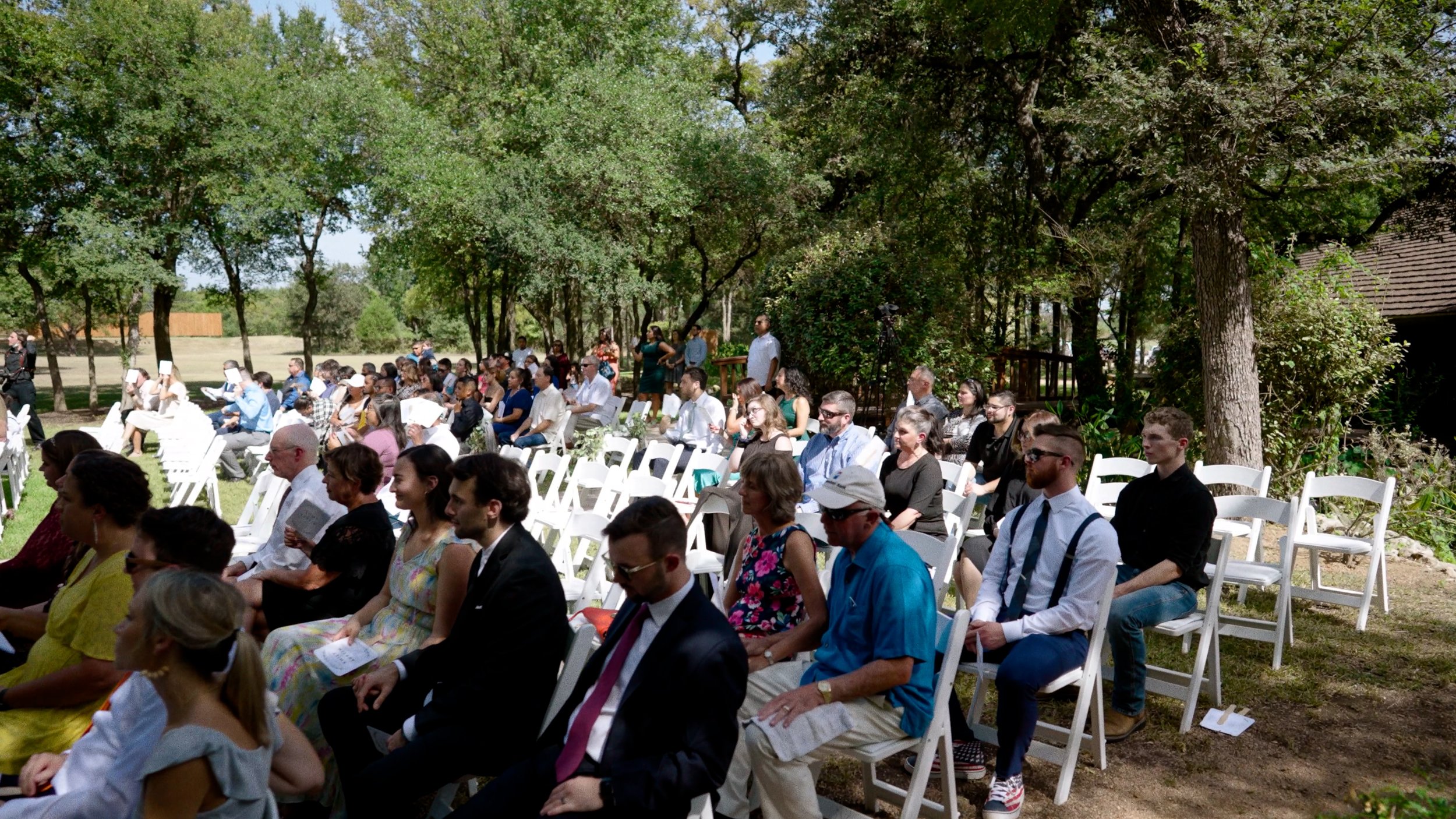wedding guests attend ceremony sitting in chairs outside on sunny day