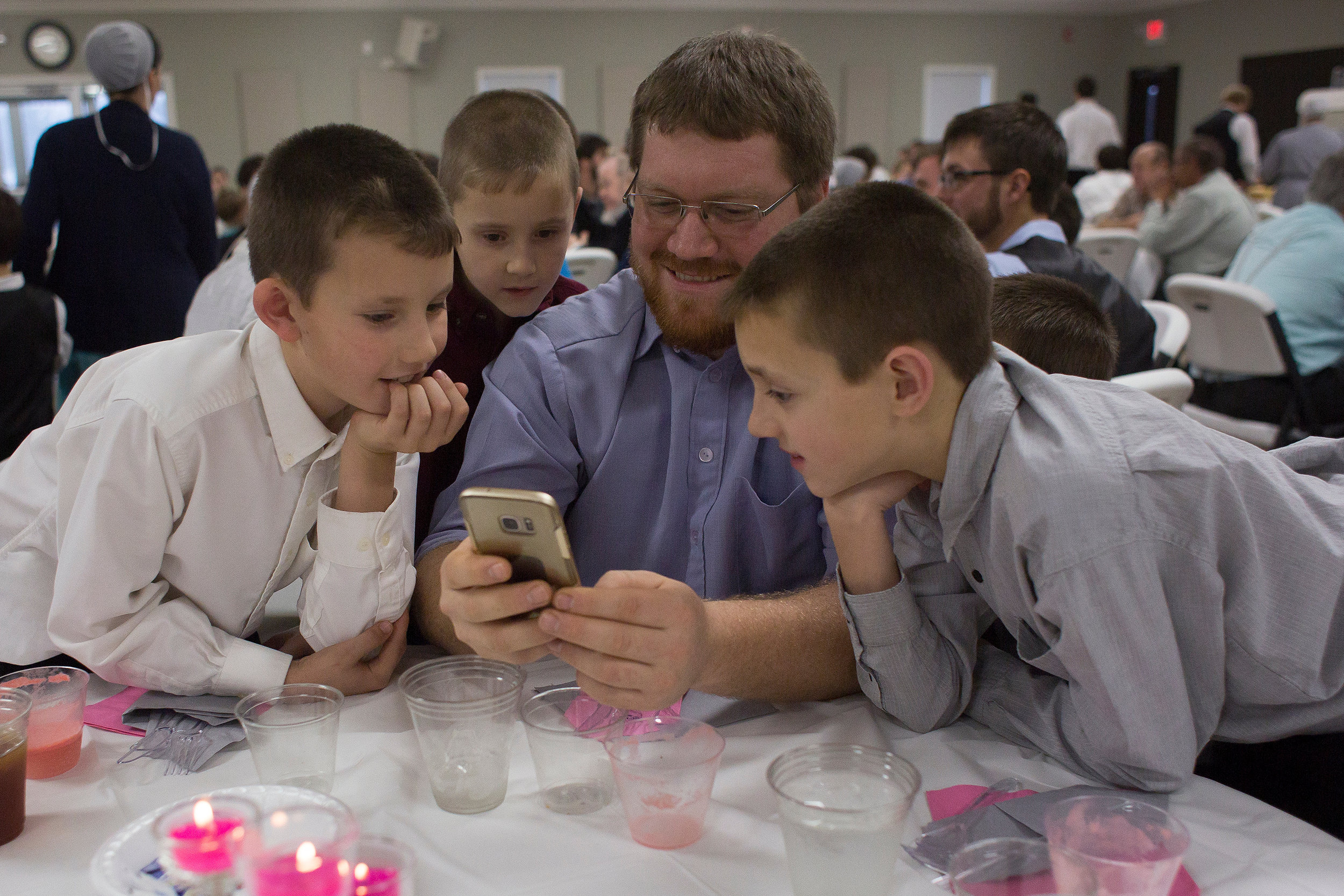  Jonathan Beachy of Flat Rock, Illinois, showed hunting videos to the Knepp children — Darius, Tyler, Zachary, and Cody — on his phone during a wedding reception Dec. 22 at Berea Mennonite Church in Cannelburg. The Knepps do not have a television or 