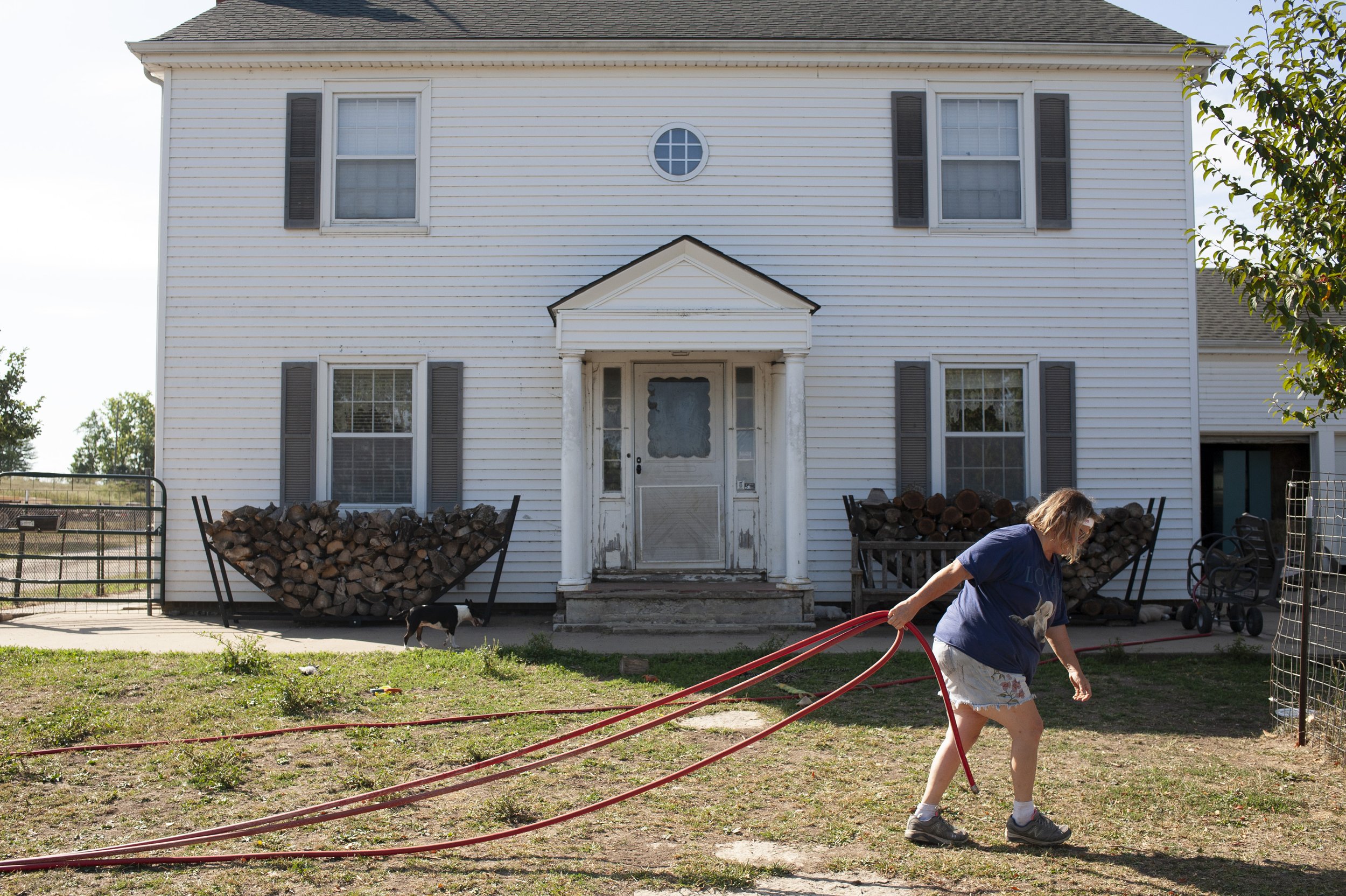  Mary pulls a hose across her front yard while tending to the morning’s tasks such as feeding and providing water for animals at her farm. 