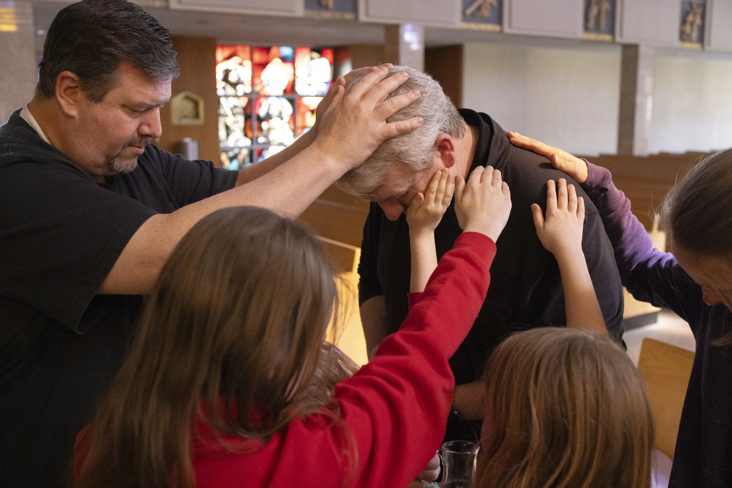  Father Brad Modde (left) placed his hands on Adam Wright during the sacrament of Anointing of the Sick on April 7 at St. Joan of Arc Church in St. Louis. Adam’s wife Beth (right) and three of their daughters, Emma, 13, Nora, 7, and Rebekah, 9, also 