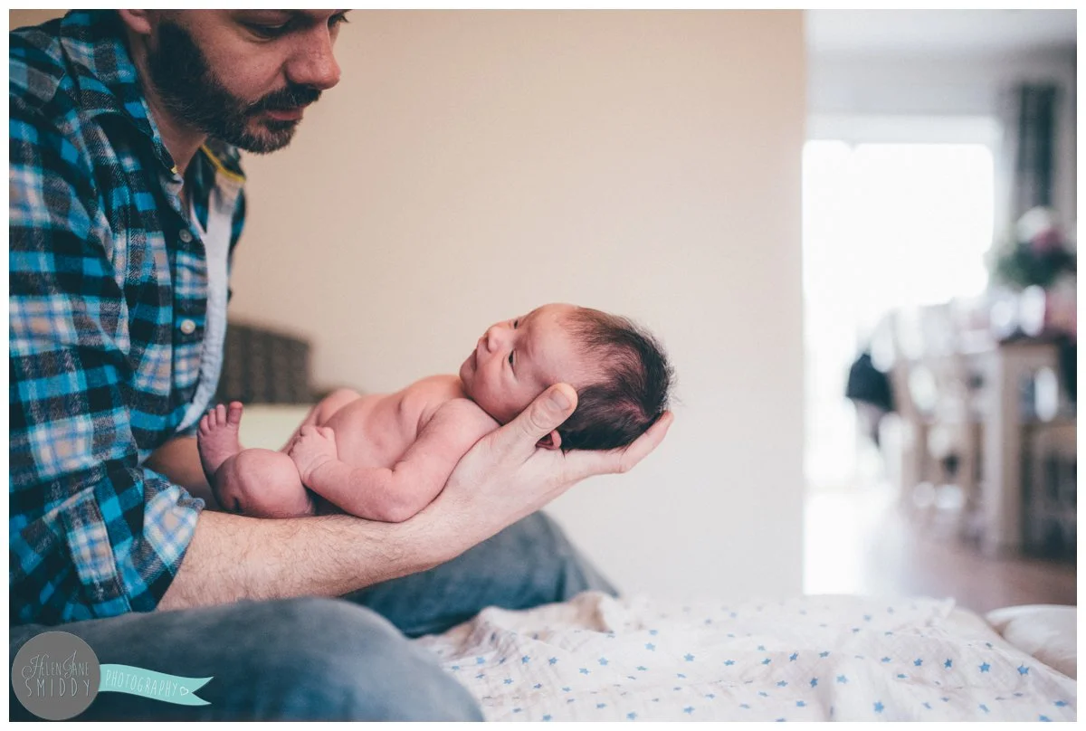 Father holds his newborn daughter in his arms for their family photoshoot.