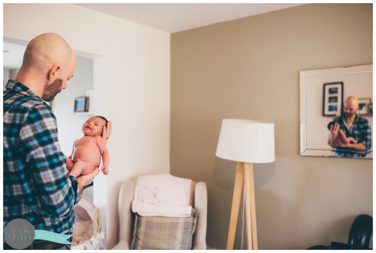 new father holds his newborn baby girl, with a reflection of them in the mirror.