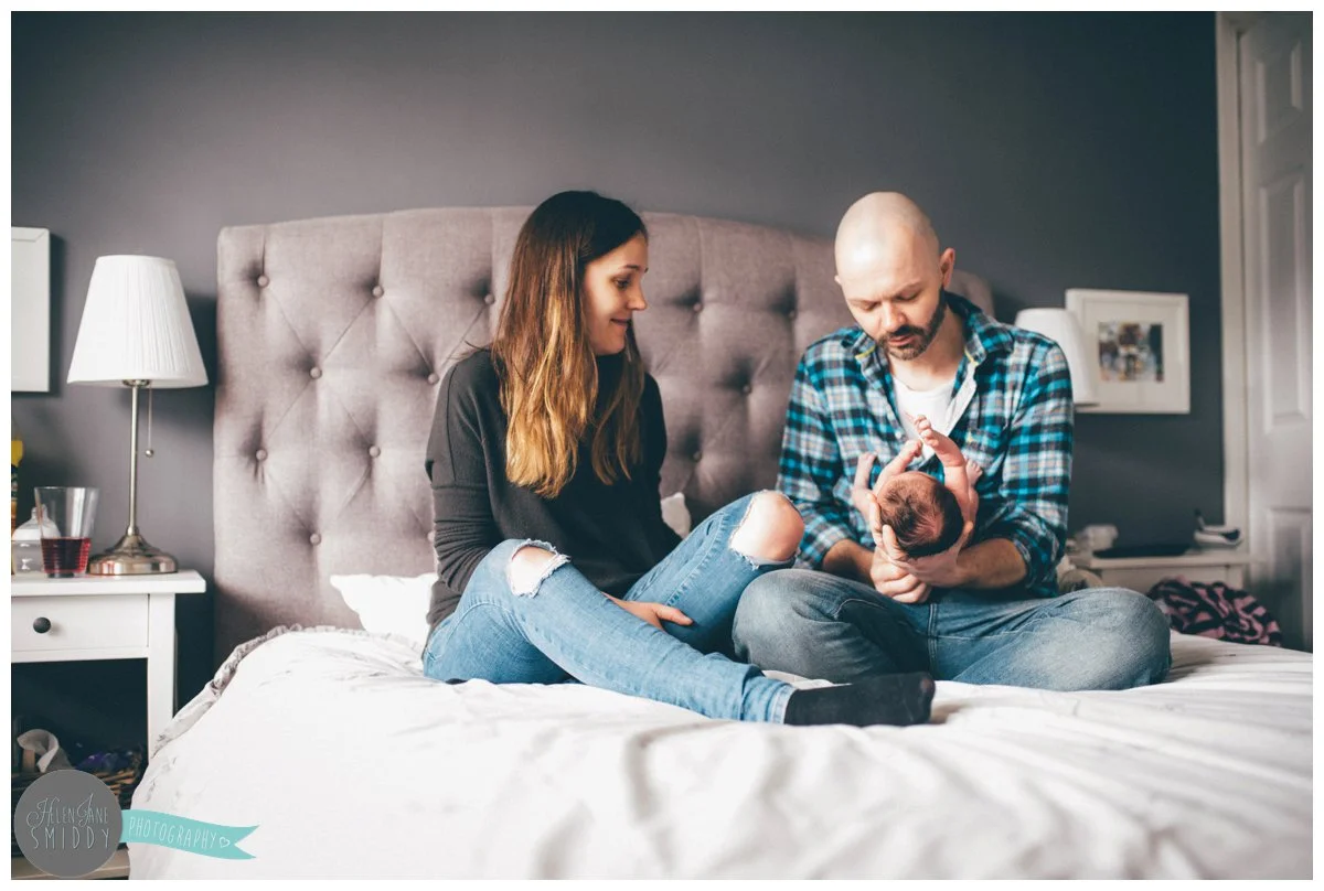 Mother and father sit on their bed with their newborn baby girl.