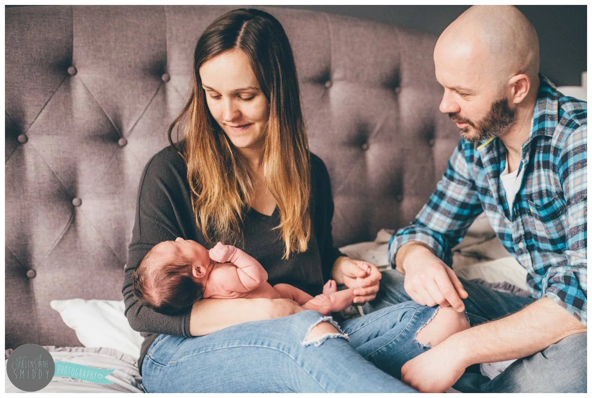 New mum holds her baby daughter whilst her husband sits next to her.