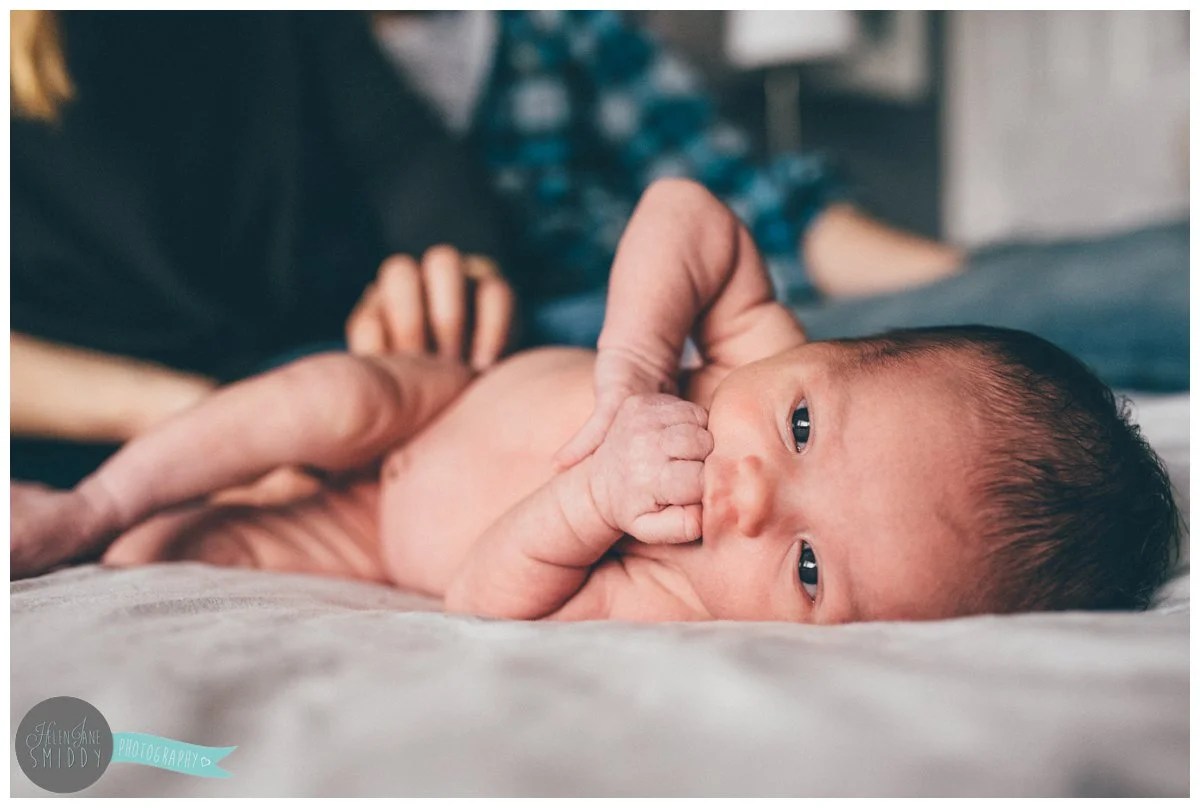 Baby girl lay naked on her mum and dad's bed falling asleep.