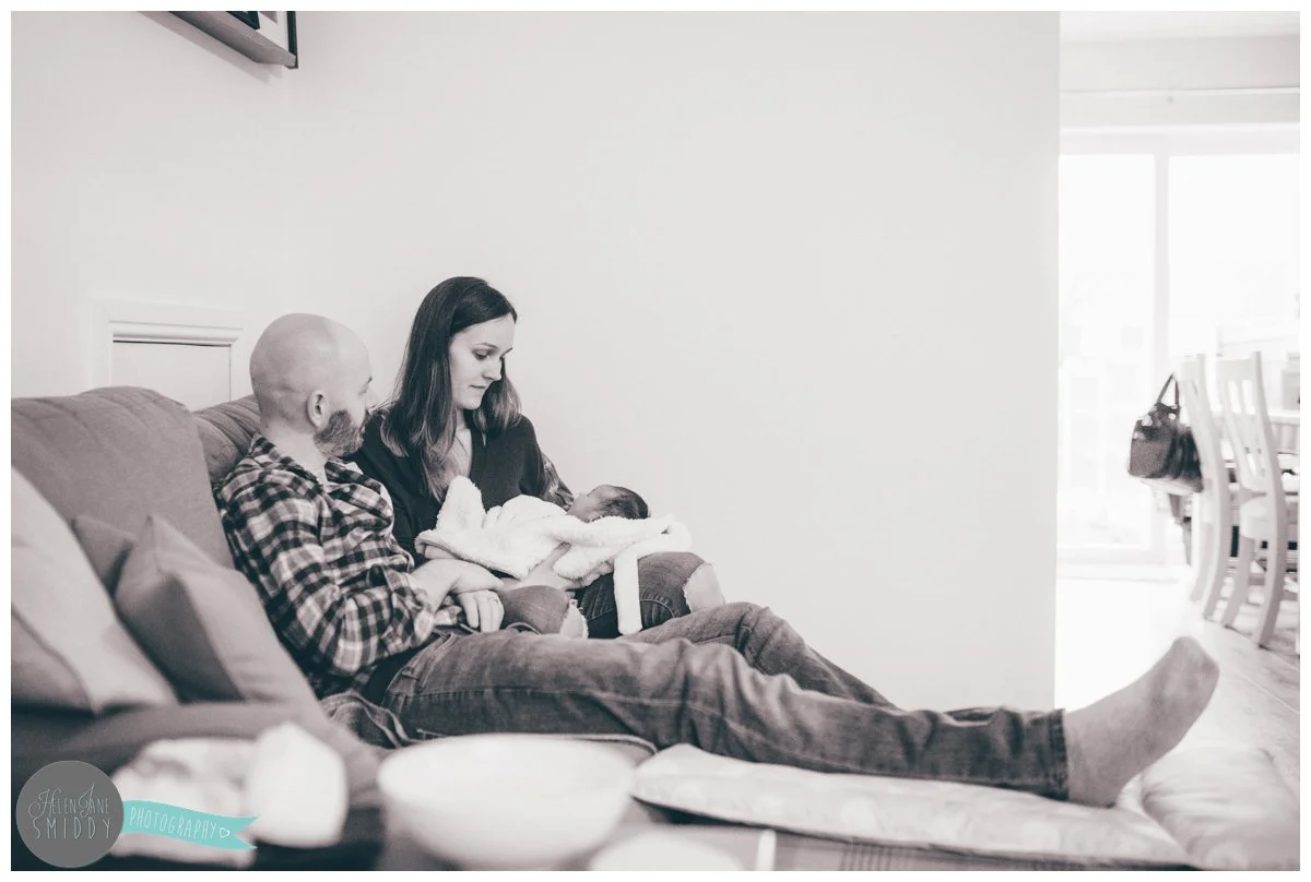 New Mum and Dad sit on the sofa in their living room in Frodsham, holding their newborn baby.