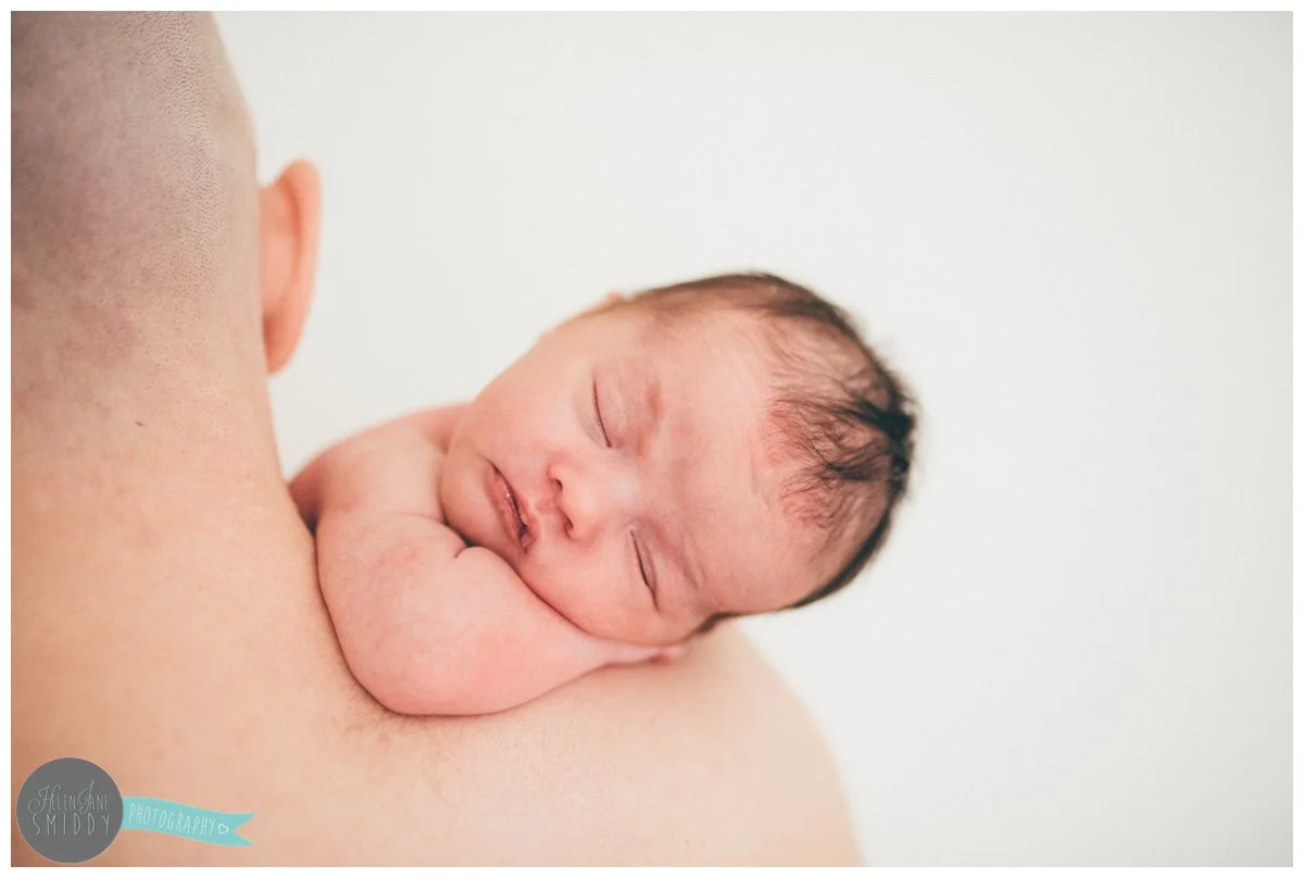 Beautiful baby girl sleeps on her Dad's shoulder in the family home in Frodsham.