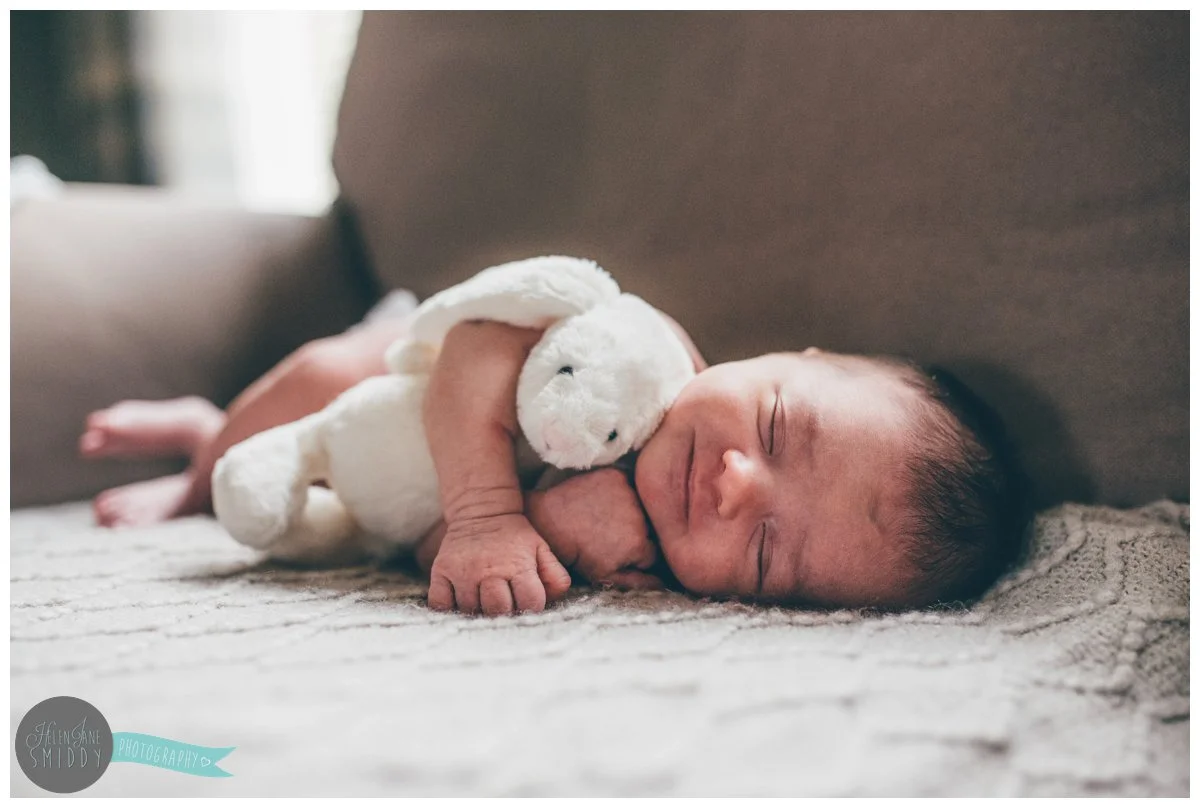 Week old baby girl smiles in her sleep whilst she cuddles her rabbit toy..