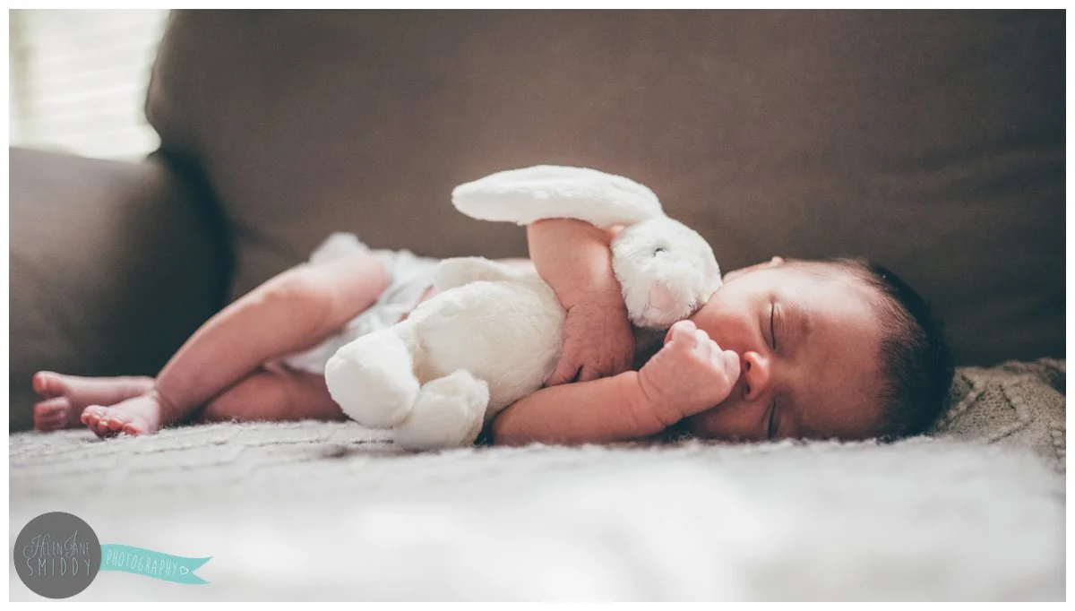 A week old baby girl cuddles her toy bunny whilst she sleeps on the sofa.
