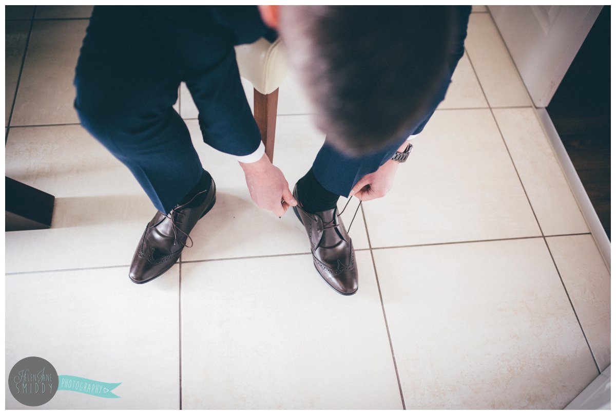 Close up of one of the best man tying the laces on his brown leather shoes.