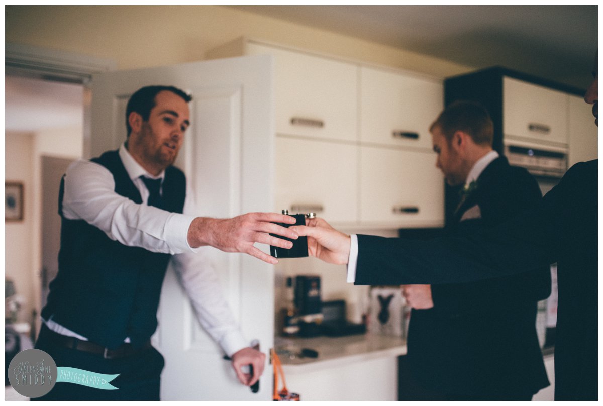 The groomsman passes the hip flask full of rum to his Best Man.