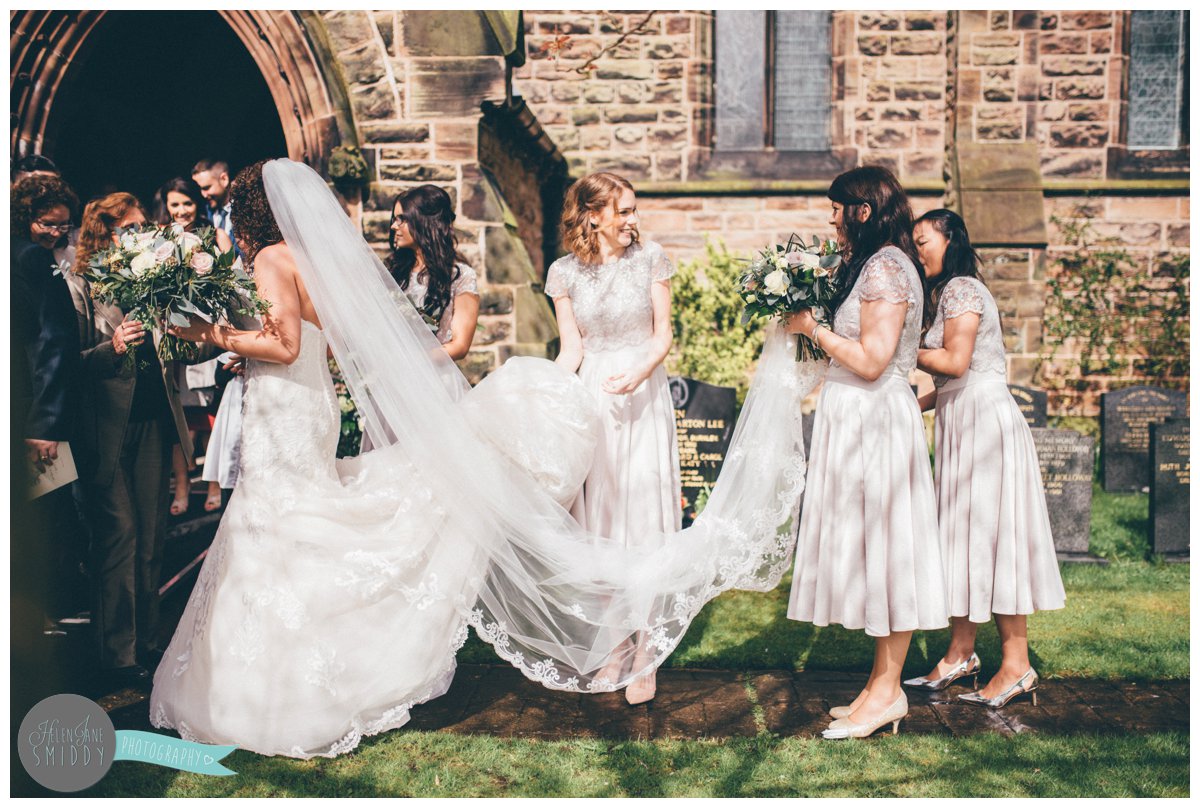 Side angle of the bridesmaids all holding the bride's beautiful gown and veil.