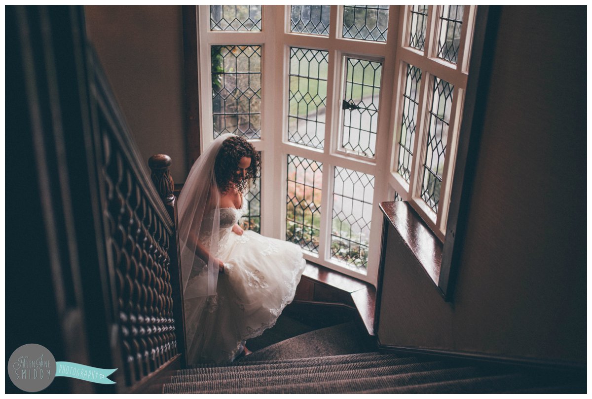 Lyssa holds her Maggie Sottero wedding gown as she walks up the stairs at Mere Court Hotel in Knutsford.