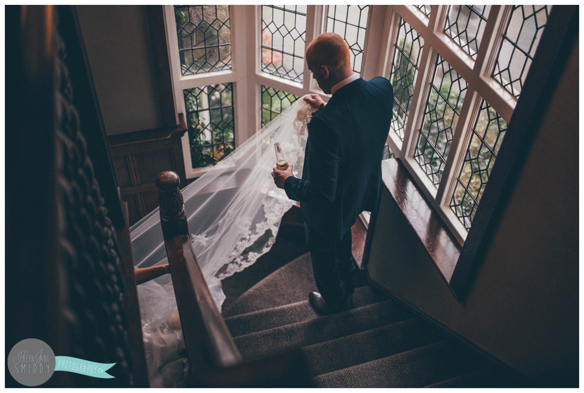 Dom holds his wife's veil and a beer as they walk back down to their wedding guests.