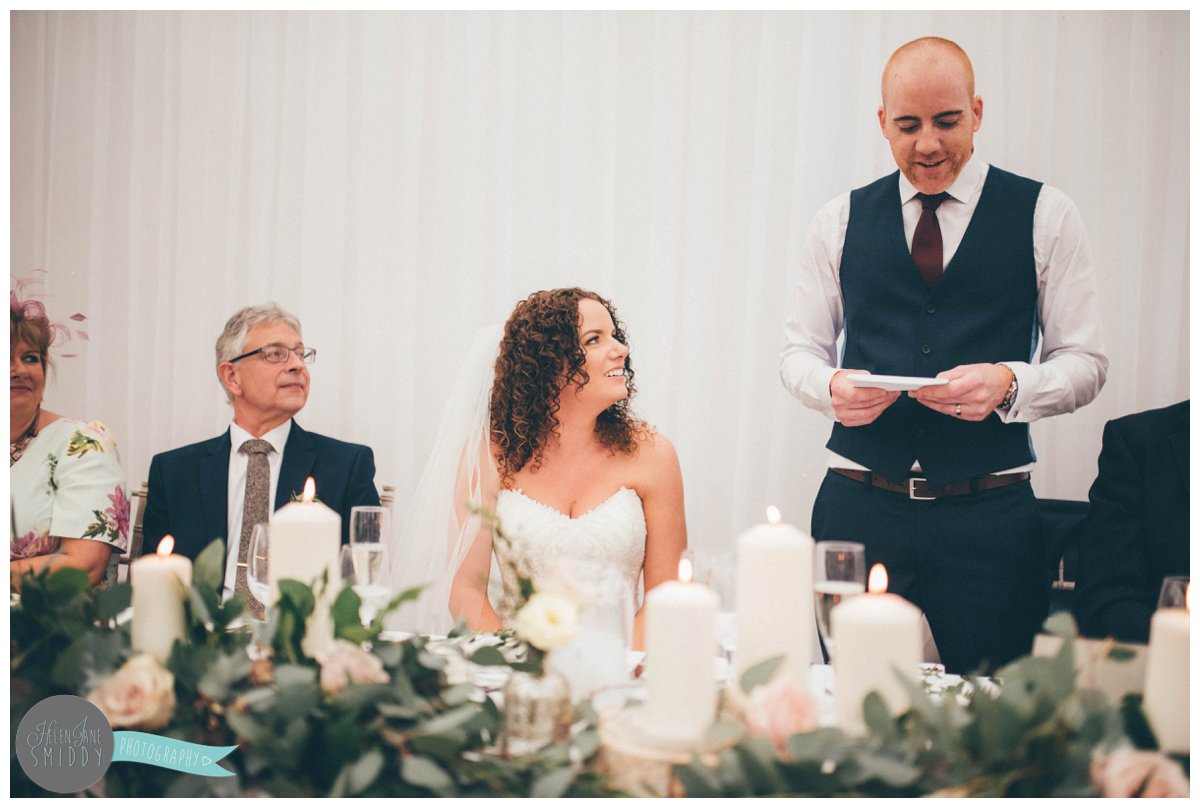 Lyssa looks at her new husband, smiling as he reds his wedding speech.