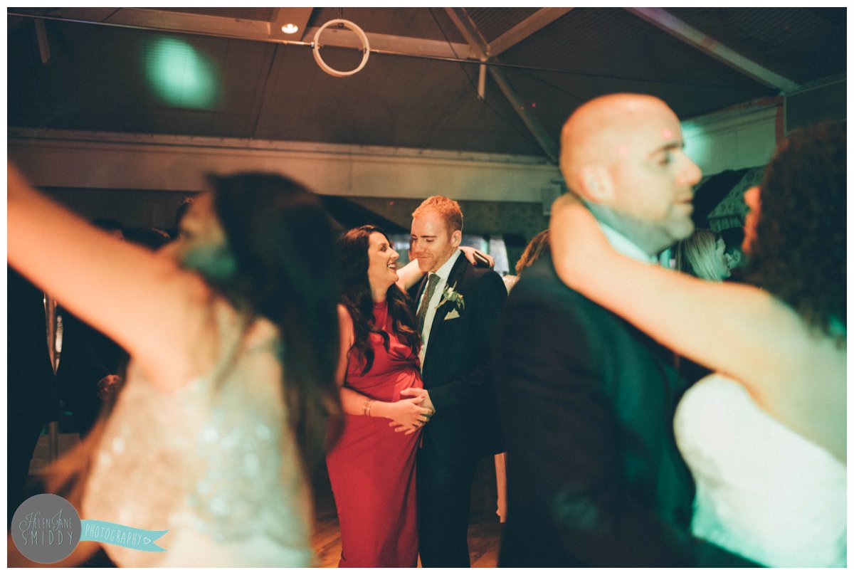 The pregnant wedding guest dances with her husband as he holds her stomach.