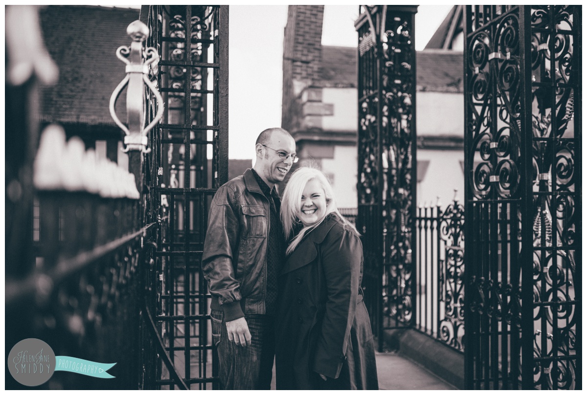 Engaged couple stand at the Eastgate Clock in Chester laughing with each other and their Cheshire wedding photographer.