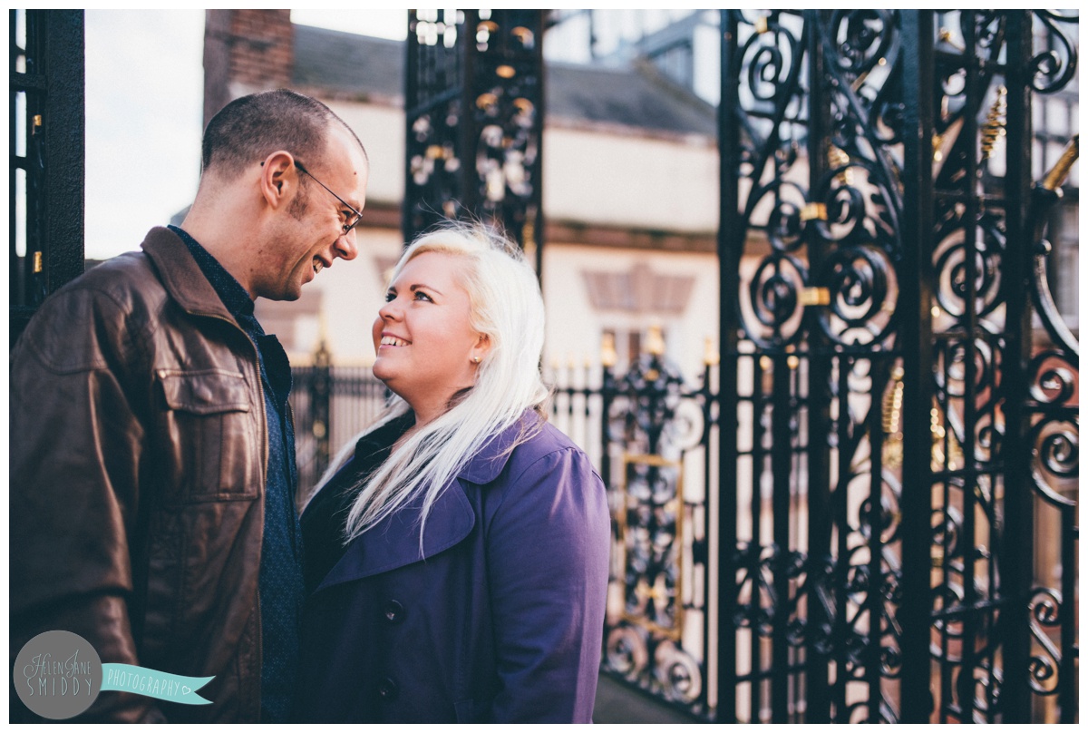 Couple stands underneath the Eastgate Clock in Chester, smiling at each other.