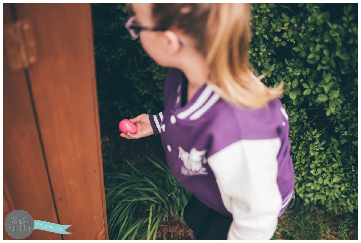 Little girl picks up a pink egg that she finds in the grass.