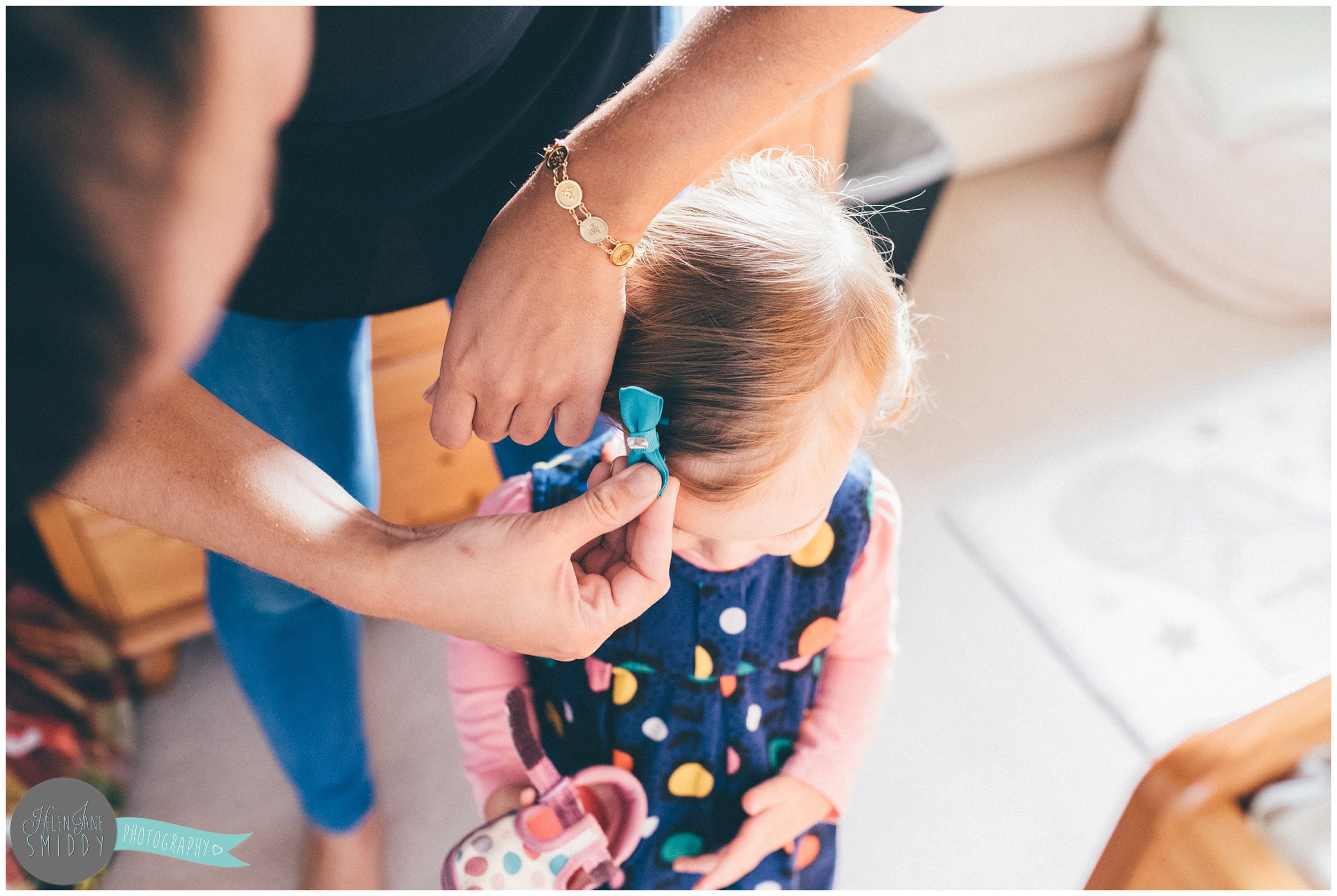 Little girl gets a bow put in her hair by her Mummy.