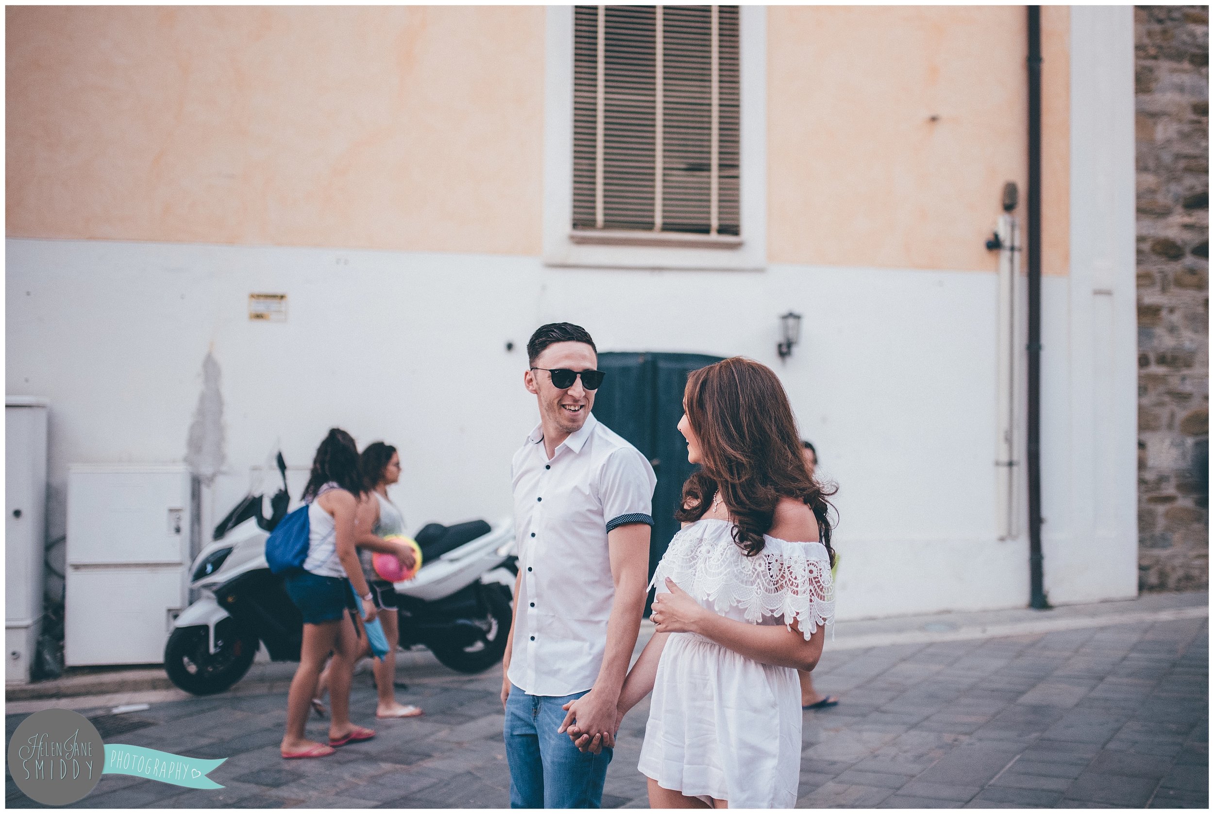The engaged couple smile at each-other whilst walking through the Italian streets.