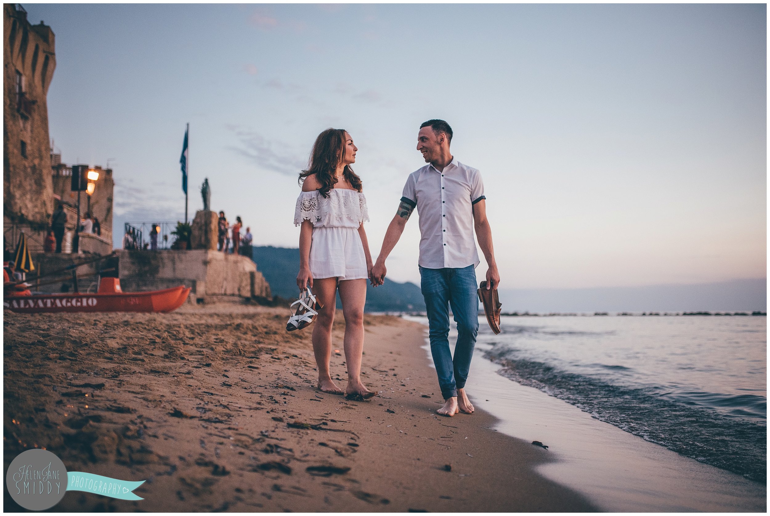 Sab and Dom stroll hand-in-hand across the beach in Italy at sunset.