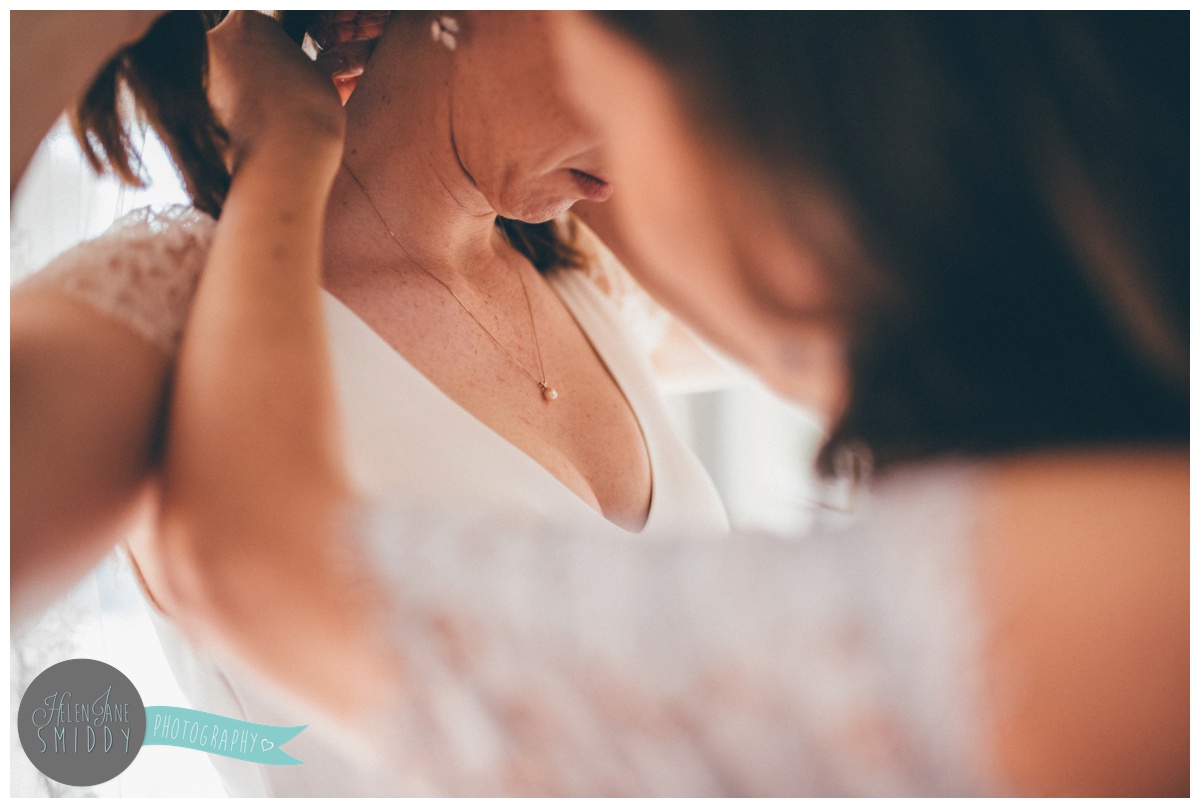 Bridesmaid helps the bride put on her pearl necklace.