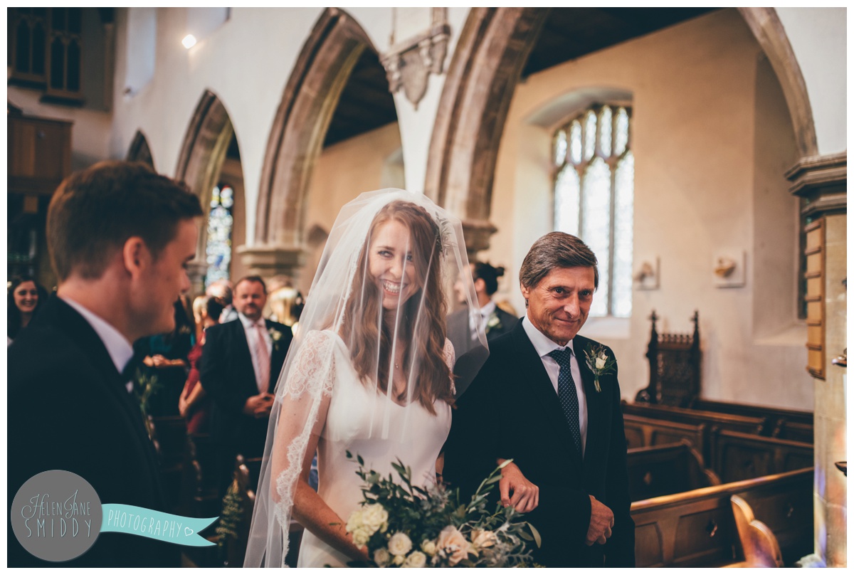 The bride beams with at her husband-to-be at the top of the aisle.