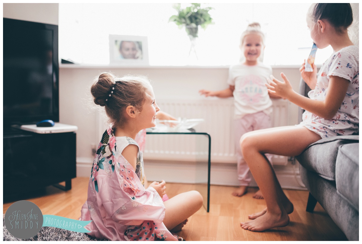 The flower girls sit together giggling in their pjs on the wedding morning.