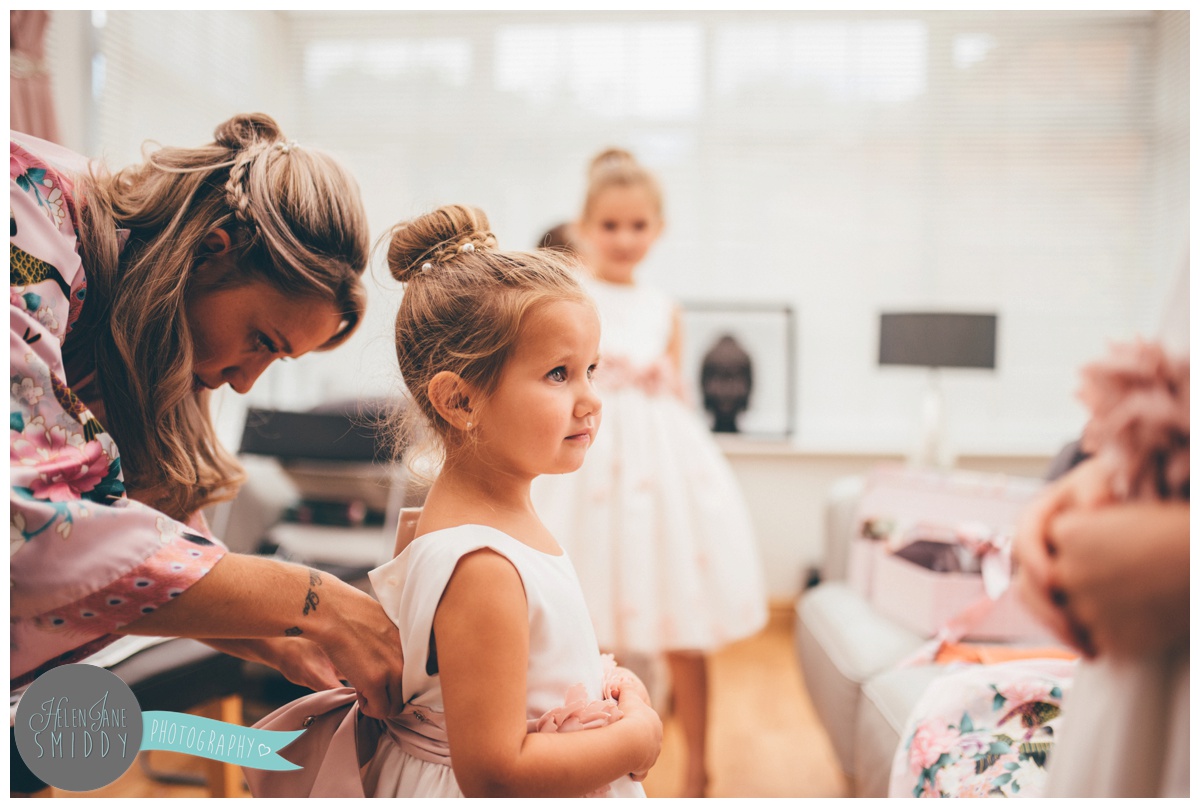 One of the older bridesmaids fastening a cute little flowergirl into her dress.