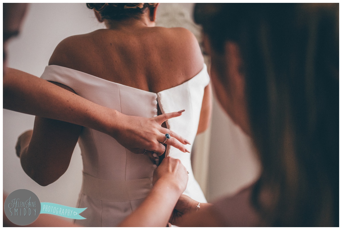 The bridesmaids button up the brides beautiful wedding gown.
