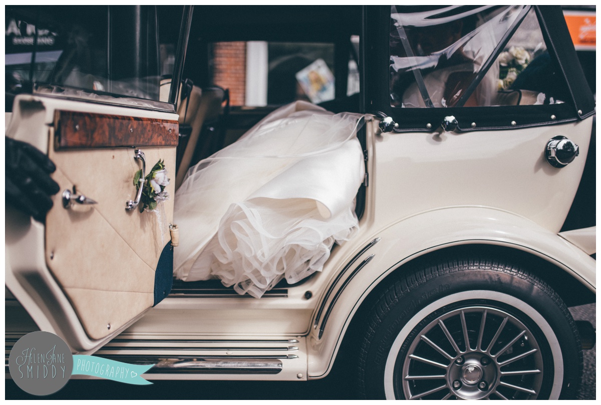 The door to the bride's wedding car is opened to reveal her wedding gown.