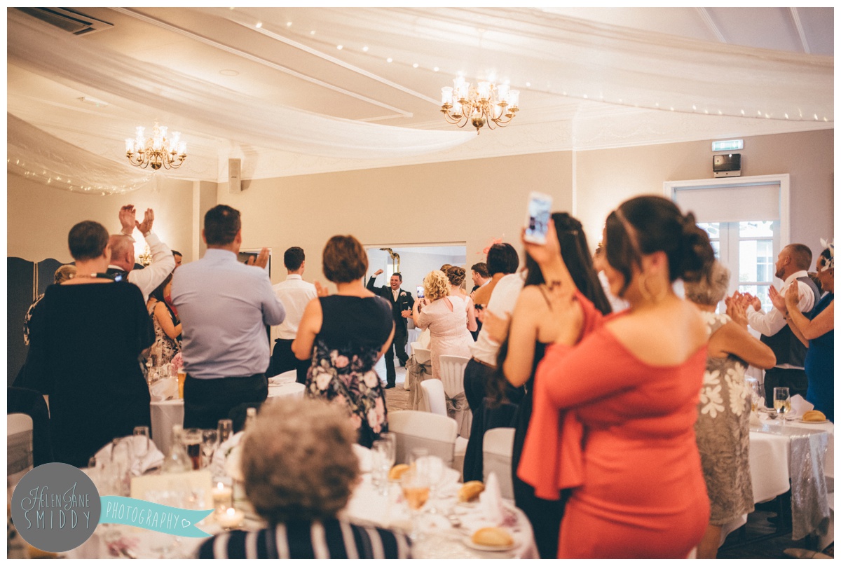 Bride and groom enter the room full of their wedding guests for their wedding breakfast at Statham Lodge..