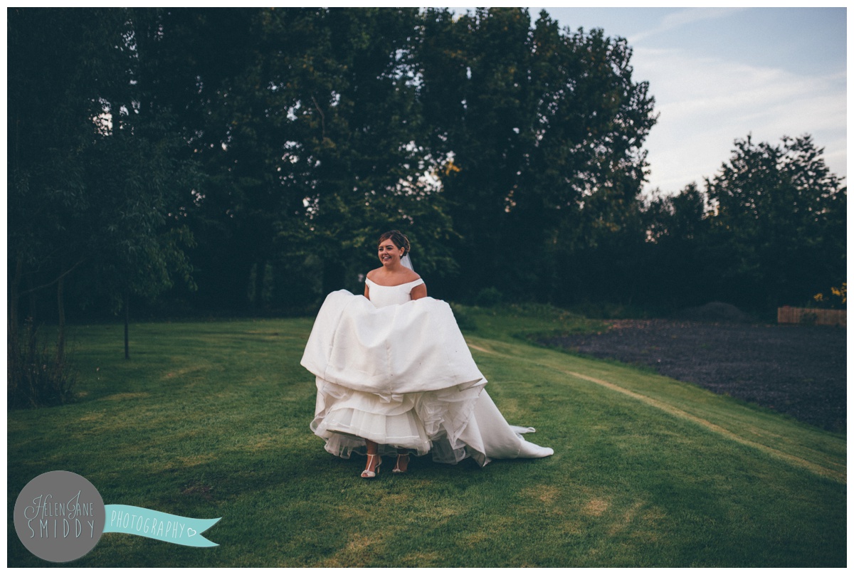 The beautiful bride walks across the grass holding her dress at Statham Lodge in Cheshire.