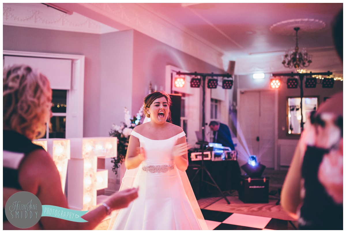The beautiful bride sings along happily on the dancefloor at Statham Lodge in Cheshire.