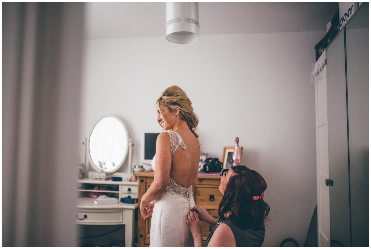 The bride's dress gets fastened up by her maid of honour.